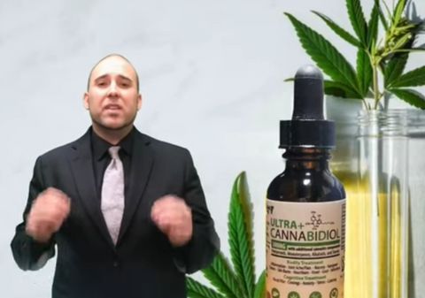 Felix is visible from the waist up in the left hand side of the frame. He is in a suit that is not properly fitted, with a black dress shirt and silver tie. He is gesticulating, and his hands are blurred by the motion. On the right side of the frame, there's an image of a tincture of CBD oil. Behind it, there are marijuana leaves and a jar of oil. These images--and Felix--are green screened in over a neutral gray background.