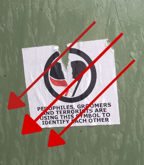 A torn sticker that says "pedophiles, groomers, and terrorists are using this symbol to identify each other" with an antifascist symbol on it. the sticker is torn