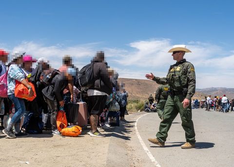 a border patrol agent in a cowboy hat gestures and smiles at a group of asylum seekers