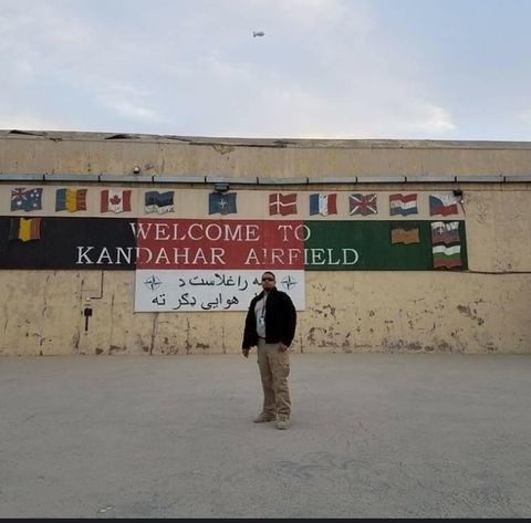a man in sunglasses standing in front of a sign that says "welcome to kandahar airfield"