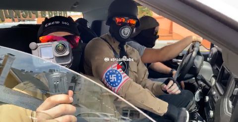 three nazis with faces covered wearing reflective sunglasses huddled together in the front seats of a vehicle