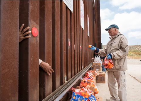 an activist hands an orange to someone through a fence