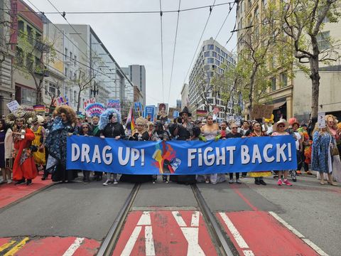 People marching in the middle of the street with a banner that says "drag up! fight back!"