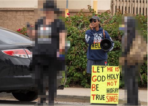 Two pride attendees confront a religious heckler. The pride attendees are pixelated to protect their identities. The heckler has a megaphone, a blue hoodie that reads "jesus saves from hell," and a sign. The sign displays the LGBT acronym like an acrostic poem, but the words comprising the acronym are altered to read "Let God Be True." The sign also reads, "He is HOLY, not HORNY SINNER."