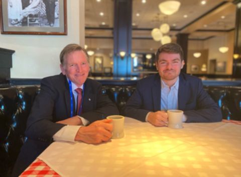 Representative Paul Gosar and Nick Fuentes both sit at a booth in a diner, both holding a coffee cup and smiling at the camera