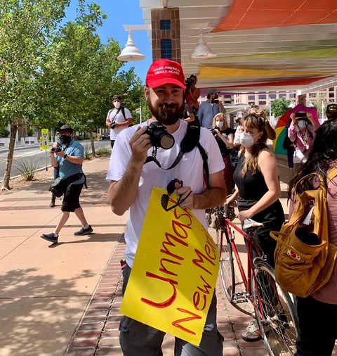 An anti-quarantine protester wearing a MAGA hat and holding a sign that reads 'Unmask New Mexico.' Photo by Bella Davis.