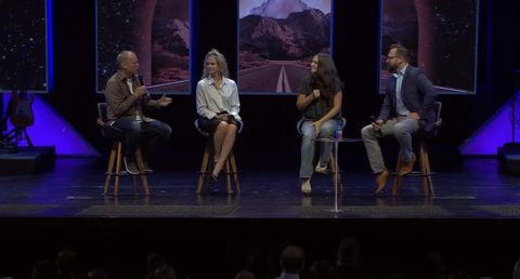 four people sit on brown chairs on a poorly lit stage with pictures of roads behind them. First is Pastor Luke Barnett in a tan shirt and blue jeans holding a microphone, next to him is his wife and co-pastor Angela Barnett wearing a skirt and shiny white blouse. Next to Angela is Debi Vanderboom with ProLife Ministry wearing a plain black shirt and blue jeans. Next to her is Josh Chumley, wearing a navy blue suit jacket and blue jeans.