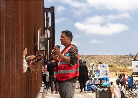 an activist hands a phone to someone through the fence
