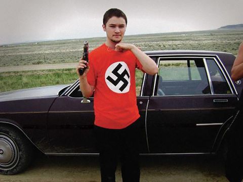 A photo of Allen Michael Goff holding a firearm and wearing a shirt with a red and white swastika symbol