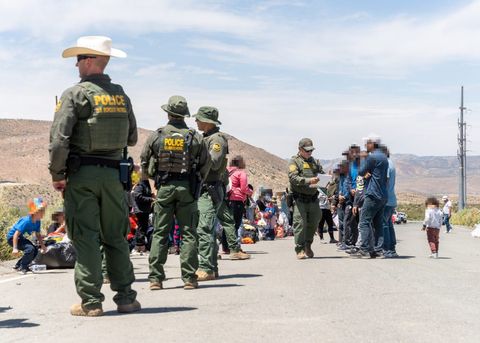 border patrol agents stand on a road, some talking to asylum seekers