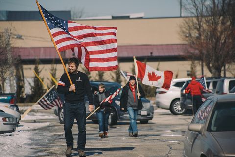 people walk toward the camera carrying canadian and american flags