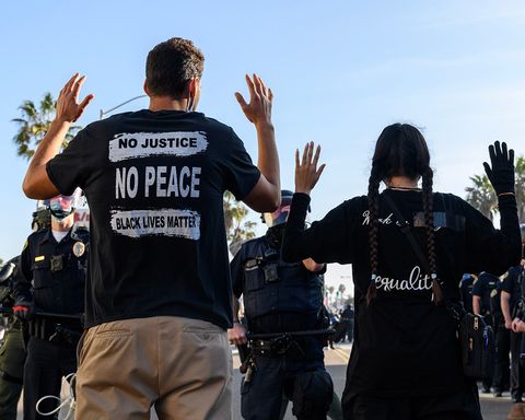 Two protestors in front of a police line with their hands up.