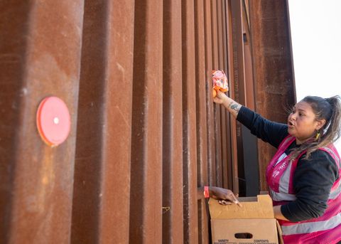 an activist hands a bag of oranges through the border fence