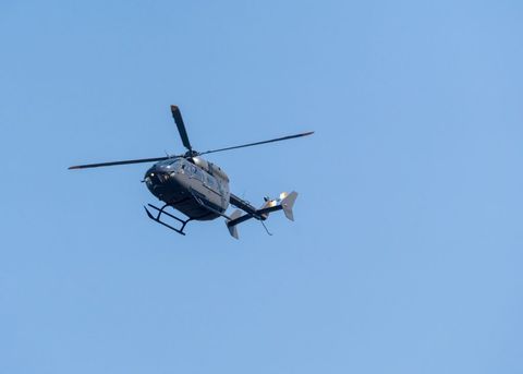 A dark gray helicopter flies overhead against a blue sky
