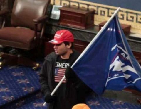 America First Bruins founder Christian Secor inside the US Capitol on January 6th. Secor appears to be wearing a 'Weimerica' T-shirt in addition to carrying the America First flag.