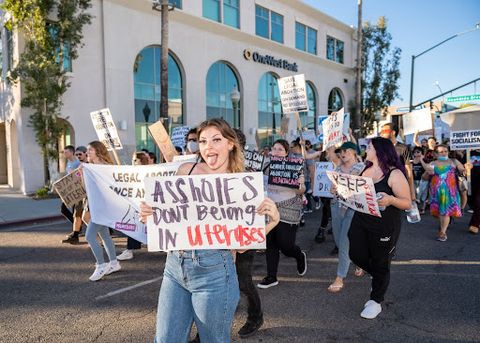A crowd of protesters marches through the streets of Escondido. One protesters holds up a sign that reads, “Assholes Don’t Belong In Uteruses.” 