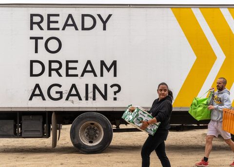 an activist caries supplies next to a van with lettering on it that says "ready to dream again?"