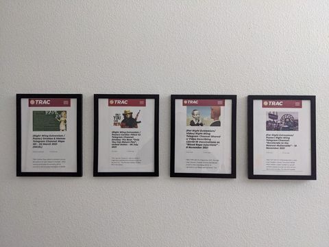 4 news bulletin articles printed out, framed, and hung on an otherwise featureless wall. A reflection in the glass of the frames reveals the photographer.