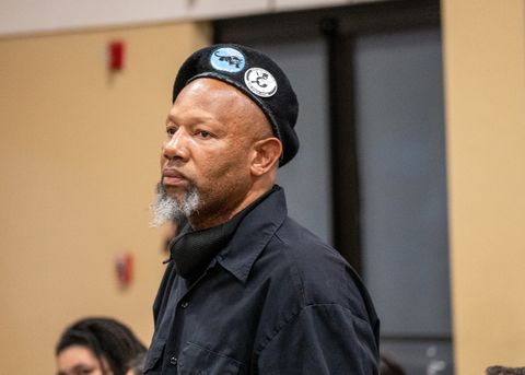 A man with a graying beard, a black beret with Black Panther pins, and a black shirt glares at Lt. Wray, who is out of frame. The man is a member of the Black Panther Party of San Diego.