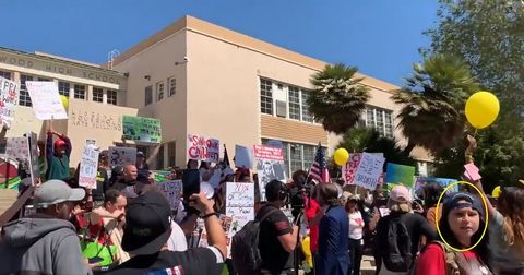 Screenshot of a video showing Kennedy Lindsey in a backwards baseball cap in the corner of the frame as a QAnon crowd gathers around Hollywood High School.