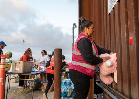 an activist hands a big stuffed bunny rabbit through the border fence