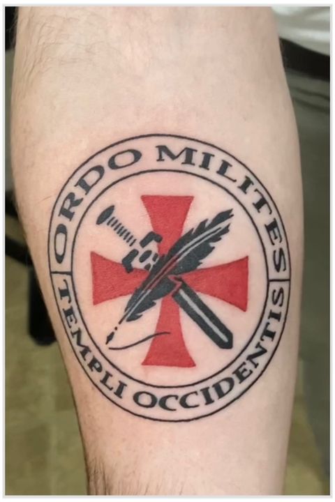 A large forearm tattoo of the OMTO logo. The logo features a black sword and a black feather overlaying a red iron cross, centered inside two black circles. The text inside the circles reads: “Ordo Milites Templi Occidentis. 