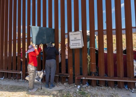 activists hand supplies through the border wall next to a sign that says "us property no trespassing"