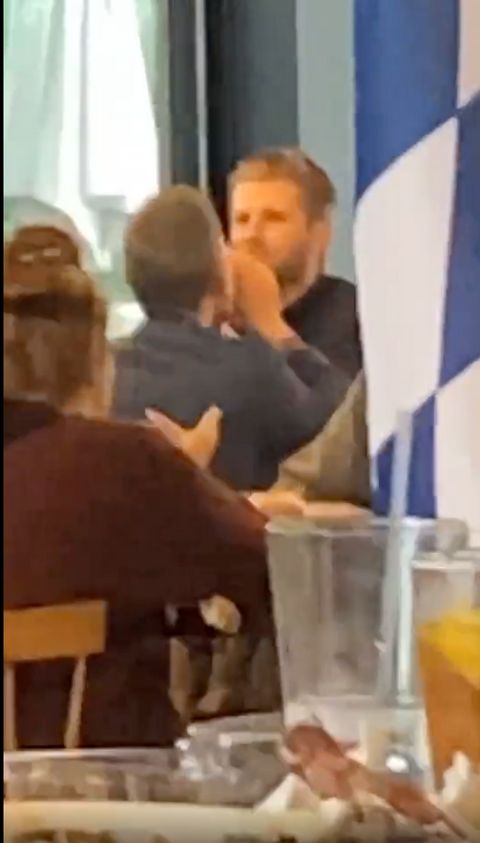 A blurry frame of a video showing a fair-skinned man in a suit eating at a table