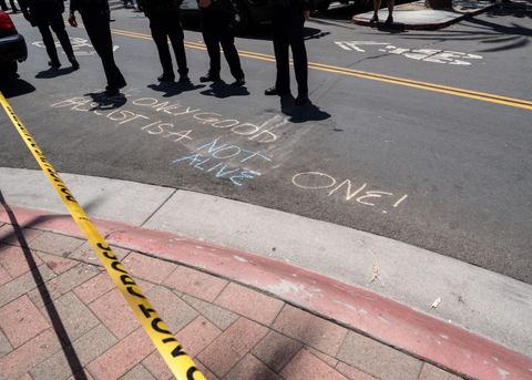 This shot is angled toward the ground. There is a chalk message on the asphalt that reads, "the only good fascist is a not alive one." The words "not alive" are written in blue. The rest are in orange.