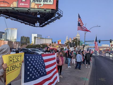 A group of 30 or so people waving flags on the side of the road in Las Vegas on a day with a blue sky