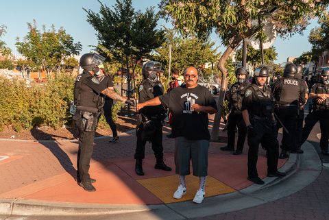 A counter-protester wearing a shirt that reads “Single Moms Matter” and depicting a dancer on a pole gives a fist bump to police officers while drinking in Martinez, Calif., on Sunday, July 12, 2020.