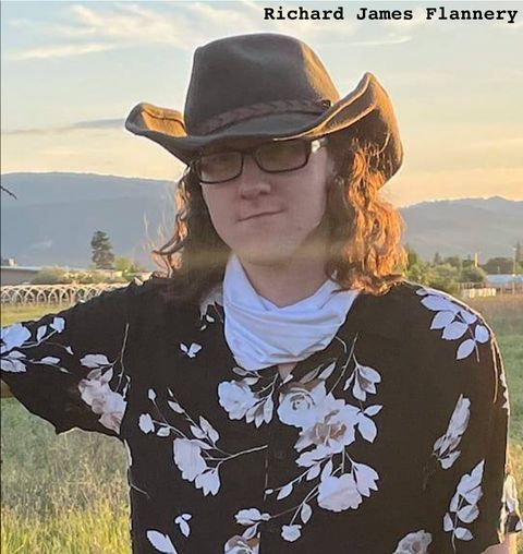 A young man with long hair in glasses and a flowery button up shirt with a cowboy hat