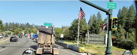Several trucks drive past a sign that says 'Welcome to Placerville, Old Hangtown'