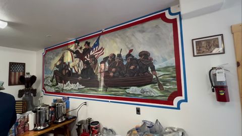 A framed painting of washington crossing the deleware holding a pizza hanging on the wall of a pizzeria