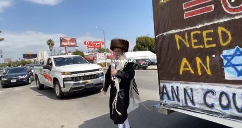 a man in orthodox jewish clothes walks toward the camera and past the GDL's u haul truck