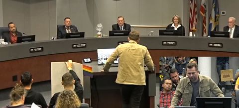 This is a screenshot of a livesteam of a Santee City Council meeting. It contains a picture-in-picture image. The main image is a shot of Samuel Deuth from behind, and a few seats in the front rows of council chambers. Beyond him, city council members are visible. In the lower right-hand corner of the image is the picture-in-picture, an image of Deuth from the front as he addresses city council. More rows of attendees are visible behind him.