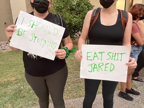 two photos of three different protest signs. The photo on the left shows two people dressed in black and wearing medical masks with signs on white paper with green text. One reads “I should be studying,” the other reads “Eat shit Jared.” The photo on the right shows one person holding a cardboard sign reading “NO RACISTS! + FASCISTS! @ ASU”